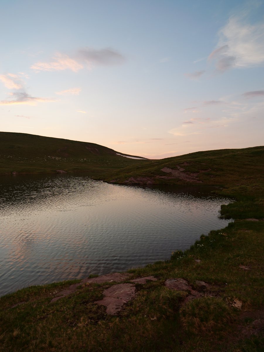Bergsee in der Dämmerung, der Himmel spiegelt sich rosa im Wasser