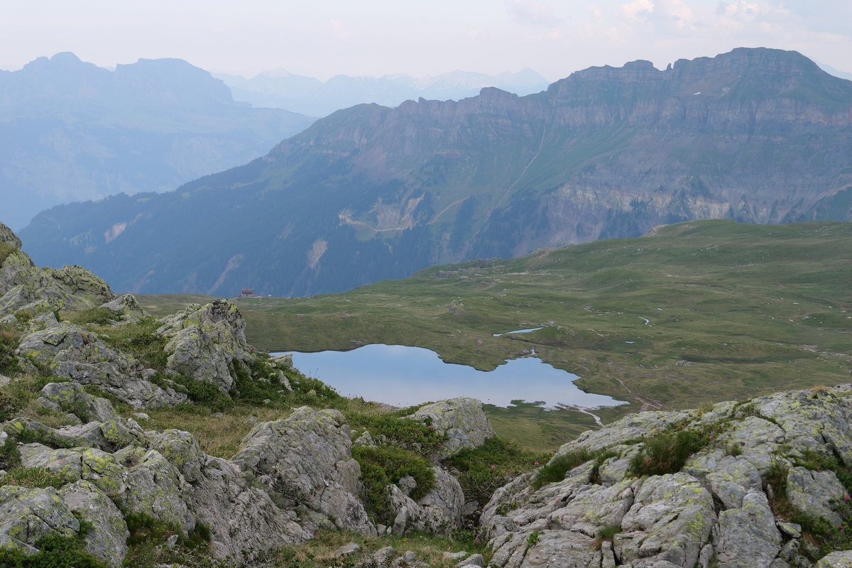 Kleiner Bergsee zwischen Kalkfelsen, dahinter eine lange Bergkette im Dunst