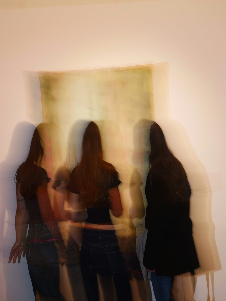Drei Personen von hinten, durch lange Belichtung verwischt, vor einem grossen hellen Bild