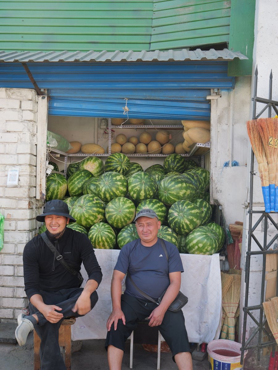 Zwei Händler sitzen lachend vor einem Berg Wassermelonen