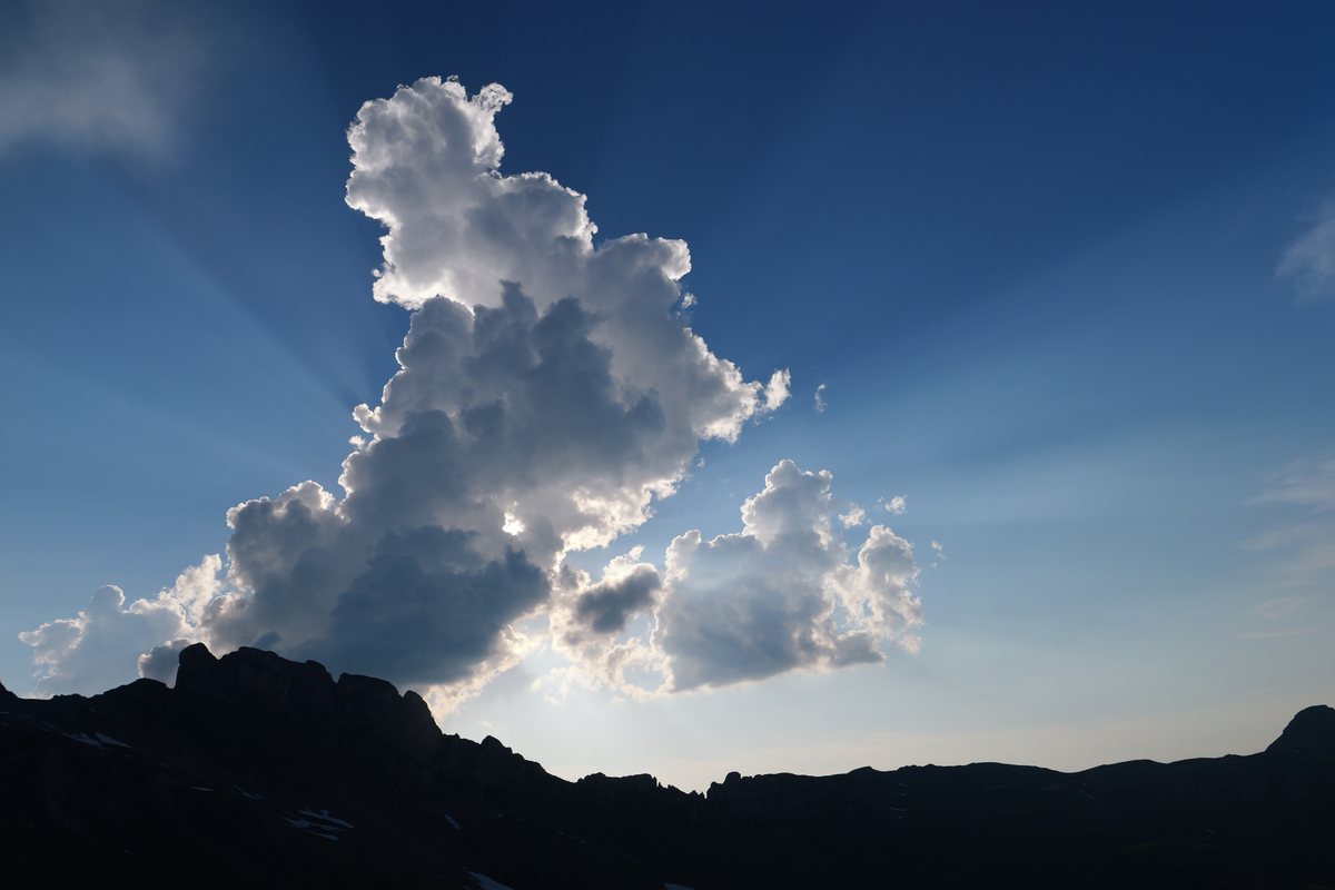 Grosse Quellwolke mit Lichtstrahlen über einer dunklen Bergsilhouette